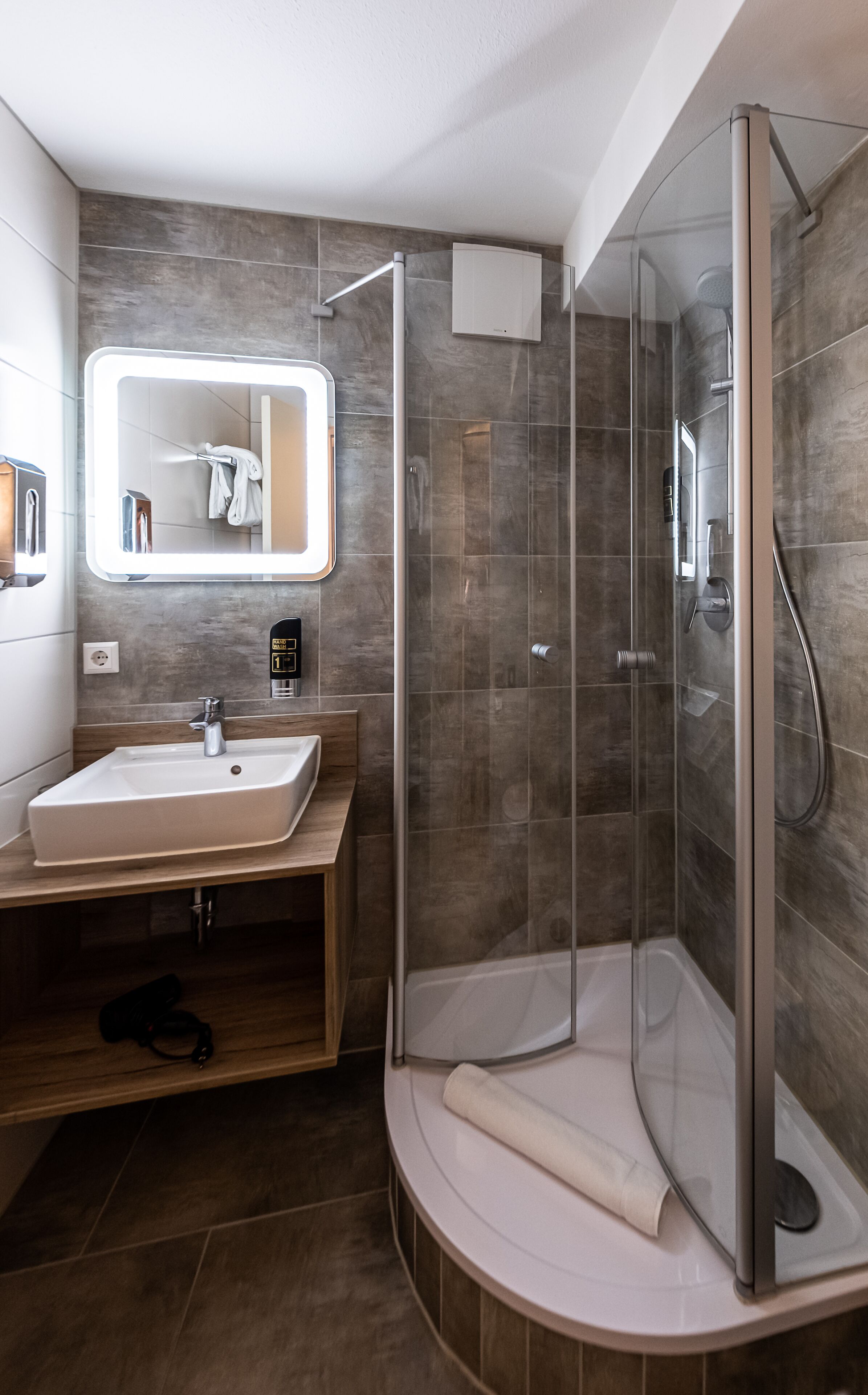 Un baño moderno con ducha acristalada, tocador con lavamanos y espejo sobre el lavamanos.