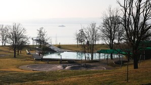 A swimming pool with a slide, surrounded by trees and a view of a body of water. - Waldhaus Jakob (Konstanz)