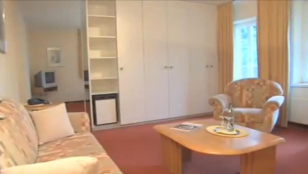 Een woonkamer met een bank, fauteuil en een bijzettafeltje. Achterin staat een garderobe en een televisie.