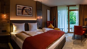 A hotel room with a large bed, a desk, a chair, and a view of the outdoors. - Waldhaus Jakob (Konstanz)