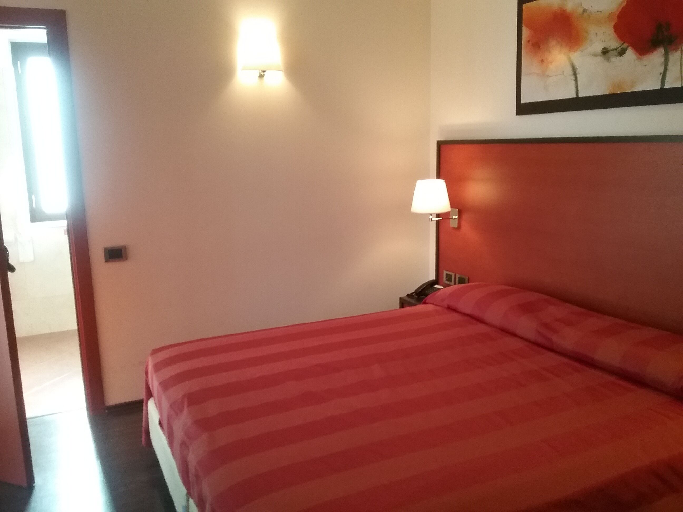 Een hotelkamer met een bed, nachtkastje, lamp en een schilderij aan de muur.