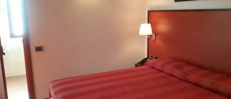Una camera d'albergo con un letto, un comodino, una lampada e un quadro appeso al muro.