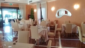 A dining area with tables set for service, a piano, and a large window with curtains. - Hotel Gullo (Curinga)
