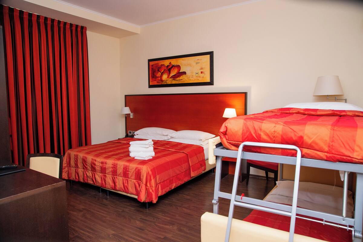 A hotel room with a large bed, a smaller bed on a platform, a desk, and a chair.