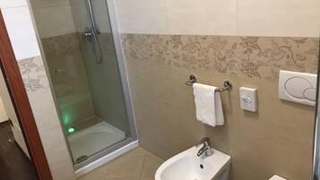 Une salle de bain avec une douche à parois de verre, un bidet et un porte-serviettes.