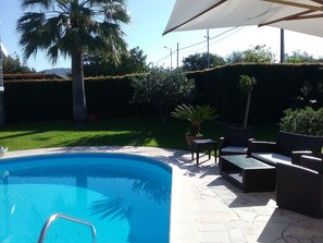 A swimming pool with a tiled deck, outdoor furniture, and a palm tree.