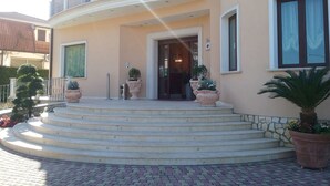 A two-story building with a curved balcony, a set of steps leading to the entrance, and potted plants. - Hotel Gullo (Curinga)