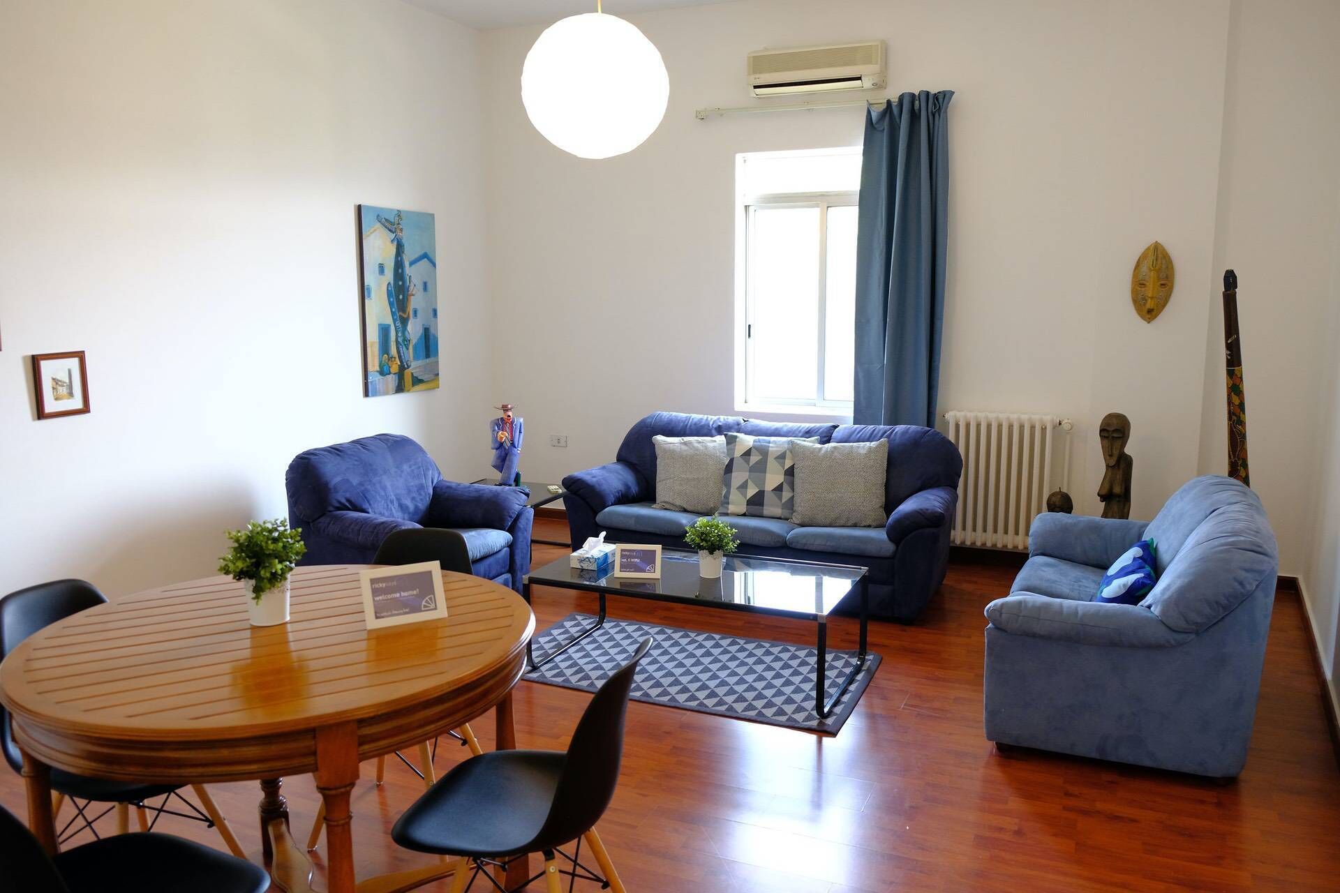 A living room with a round wooden table, two blue sofas, a coffee table, and a radiator.