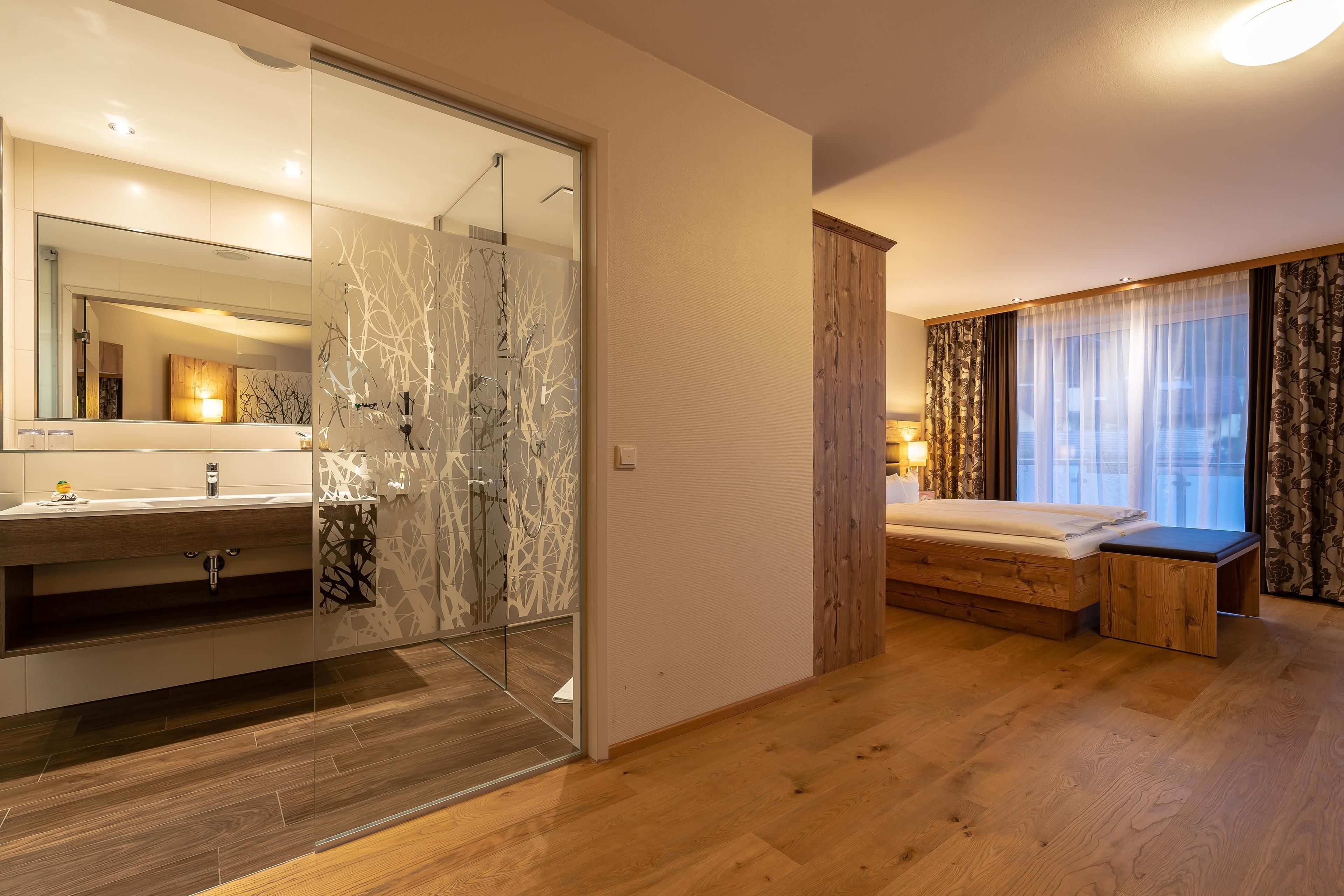Ein modernes Schlafzimmer mit Holzboden, einem großen Bett, einem Holzschrank und einer Duschkabine aus Glas.