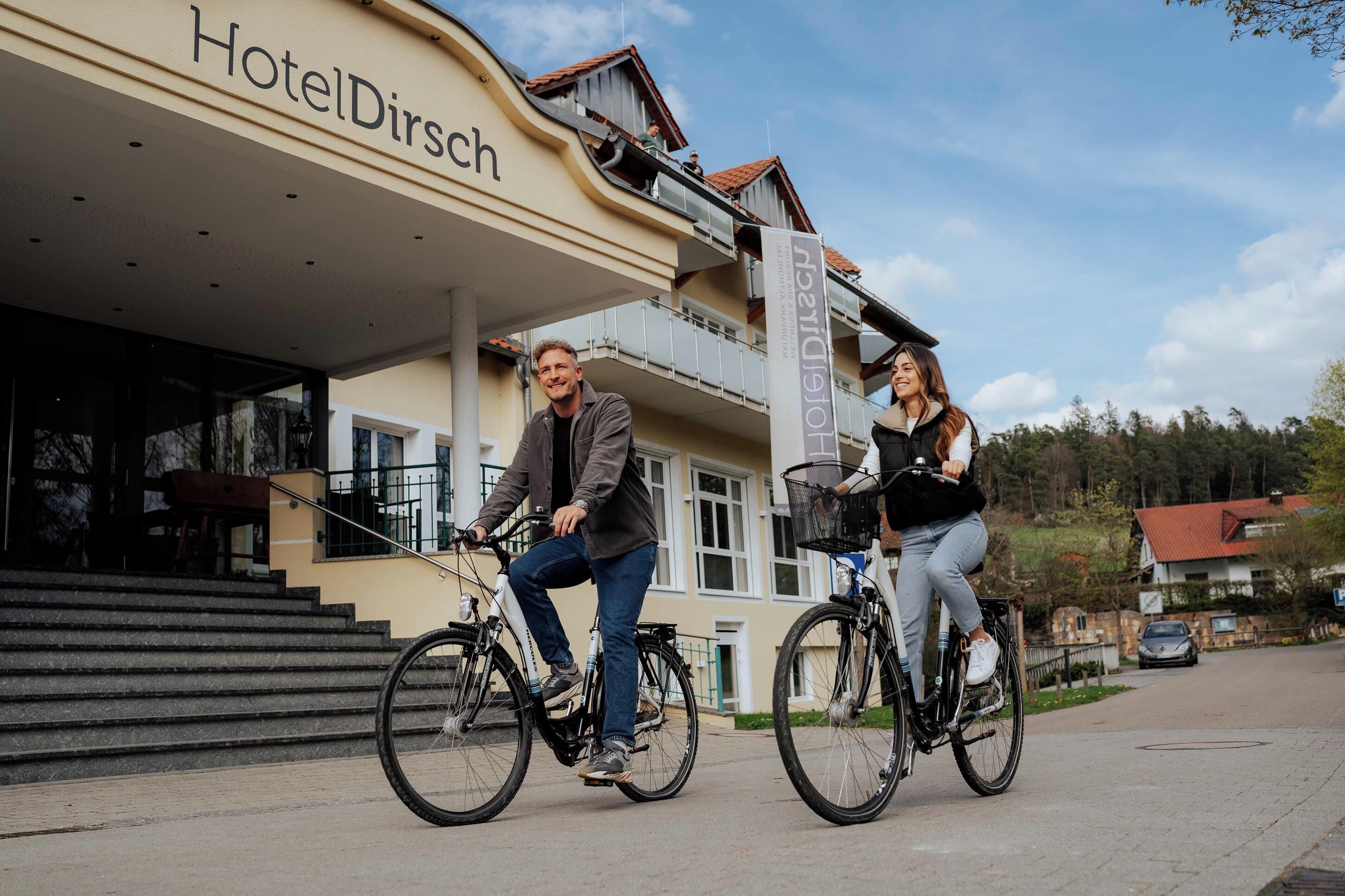 Two people riding bicycles in front of a building labeled "HotelDirsch."