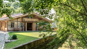 Una casa de madera con balcón, un muro de piedra y un patio cubierto de césped.