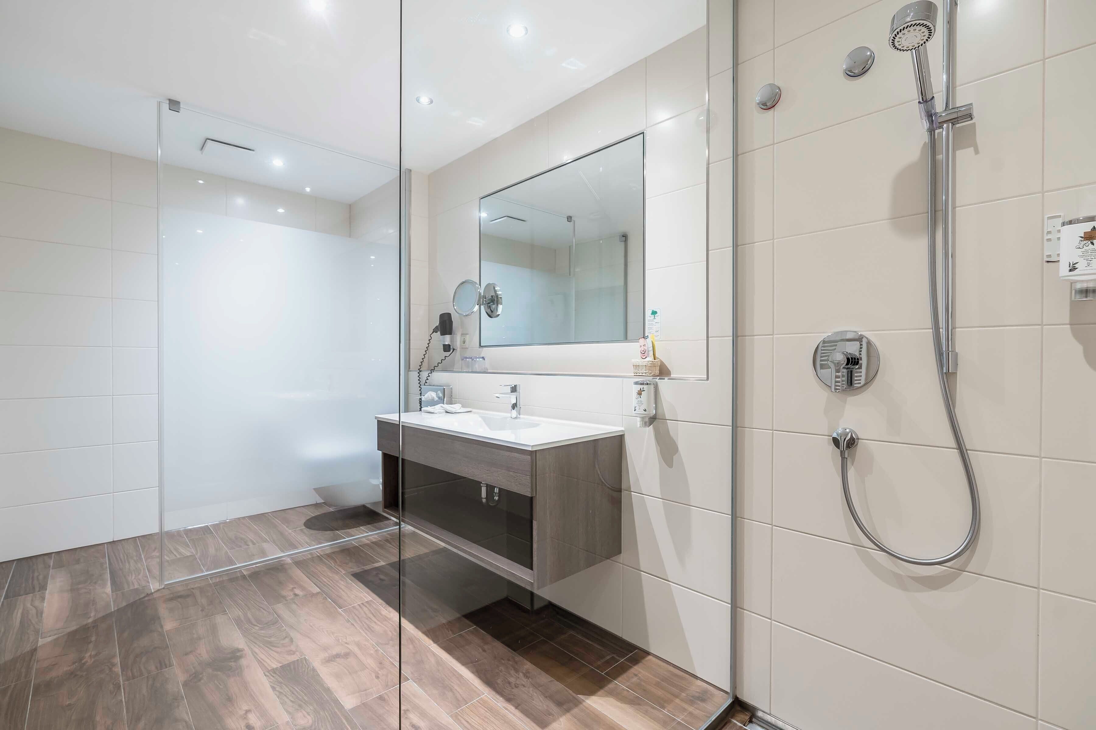 Un baño moderno con cabina de ducha de vidrio, un espejo grande y un tocador con lavamanos y perchero.