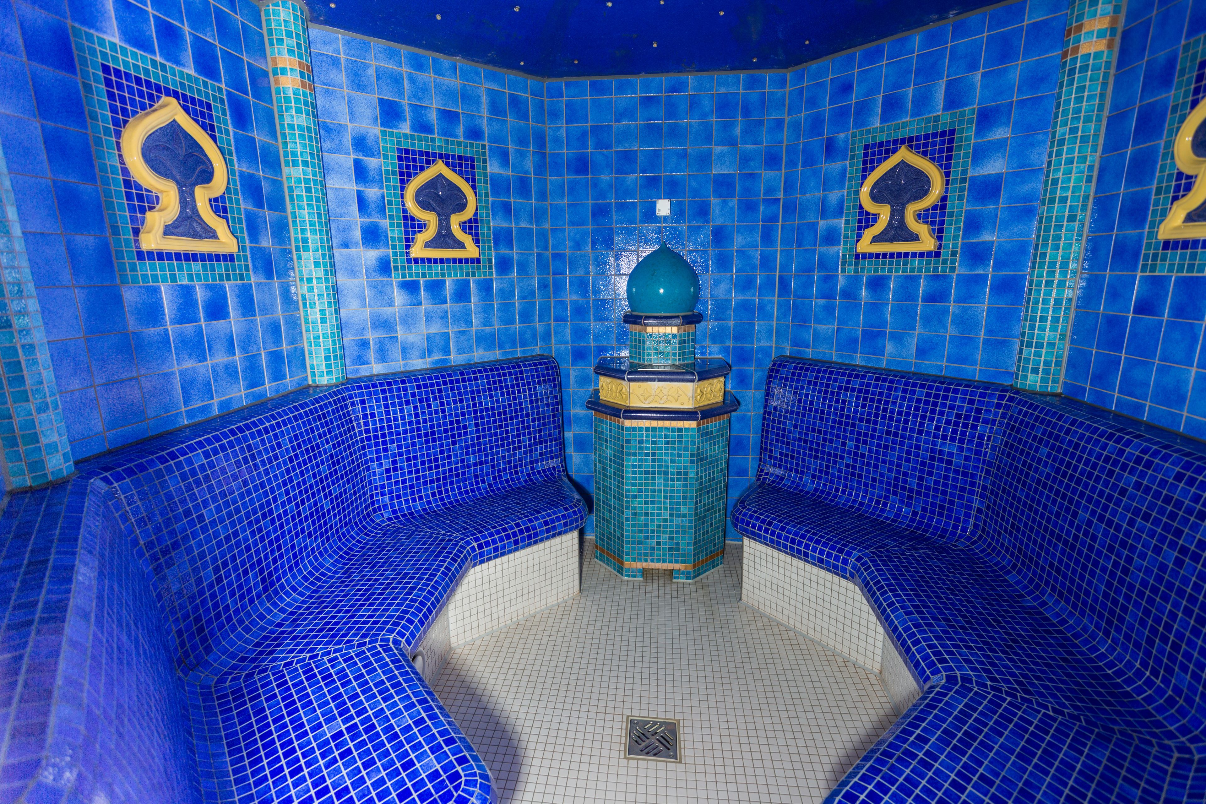 A blue-tiled room with a central column and two seating areas.