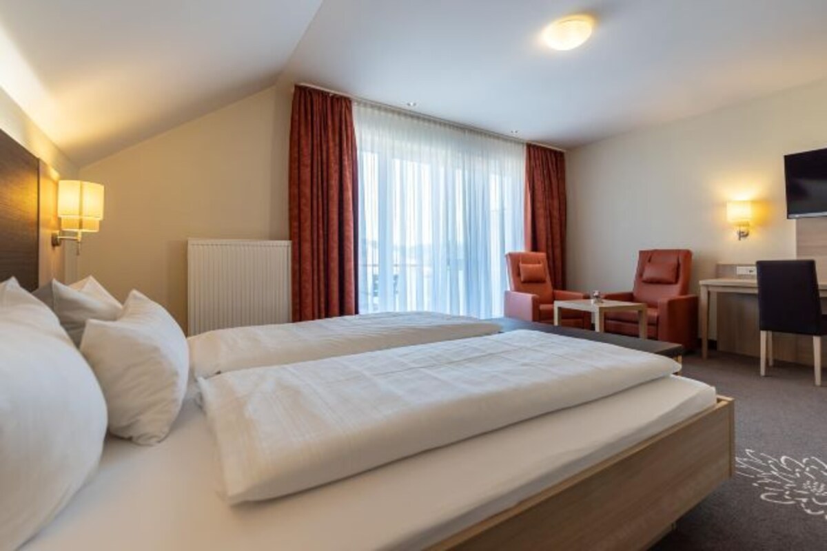 A hotel room with two beds, a desk, a chair, and a television.