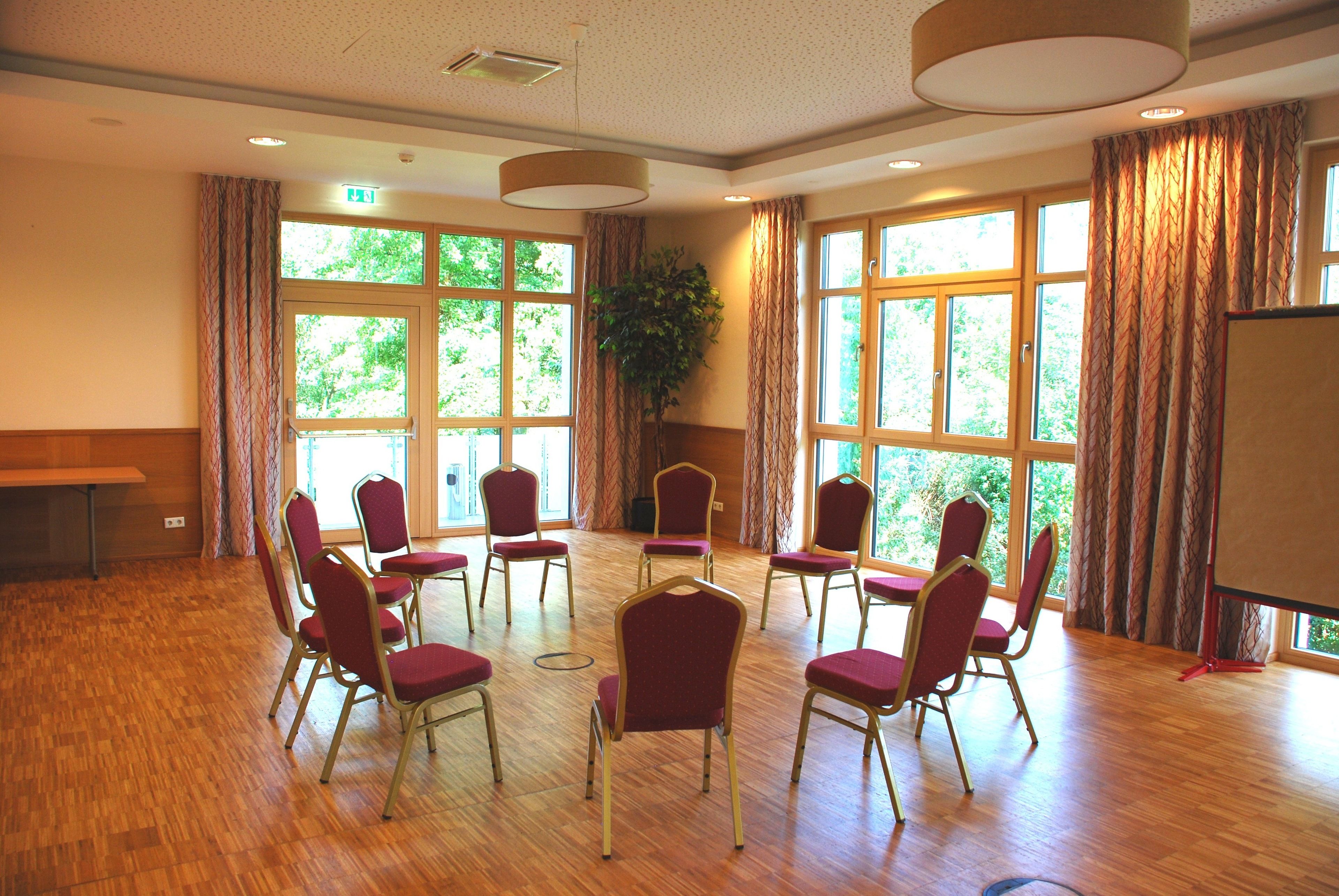 A conference room with wooden floors, red chairs, large windows, and a plant.