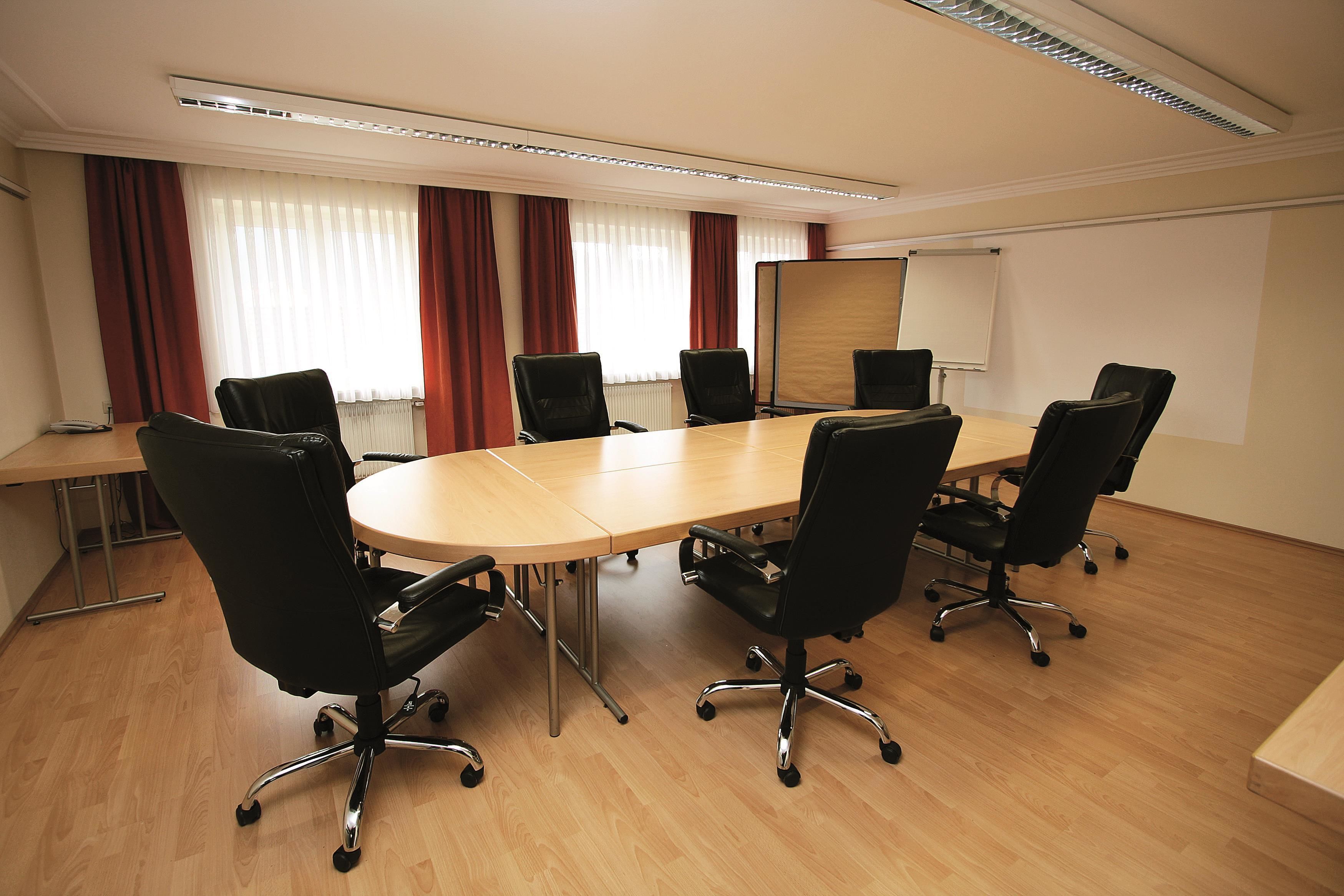 Een vergaderzaal met een grote tafel, zes zwarte bureaustoelen, een whiteboard en een projectiescherm.
