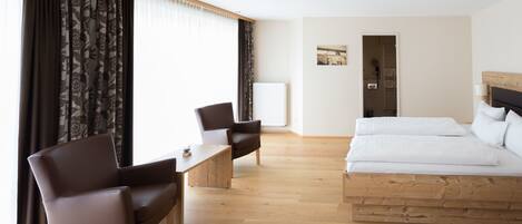 A modern hotel room with a wooden bed, a desk, a chair, and a large window with curtains.
