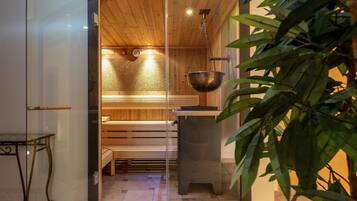 A sauna room with wooden benches, a hanging metal basin, and a glass partition.