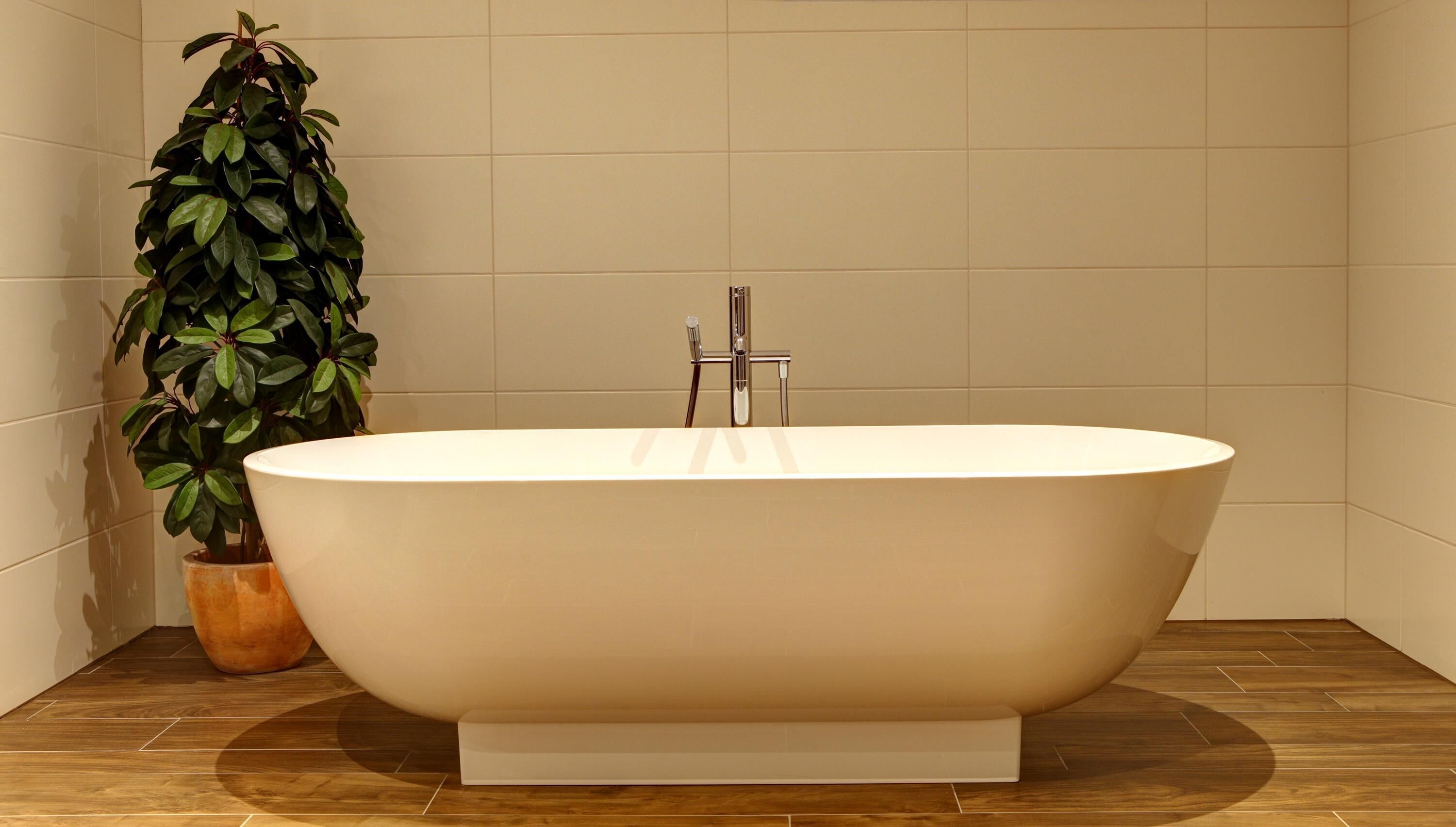A freestanding bathtub in a bathroom with a tiled floor and a potted plant.