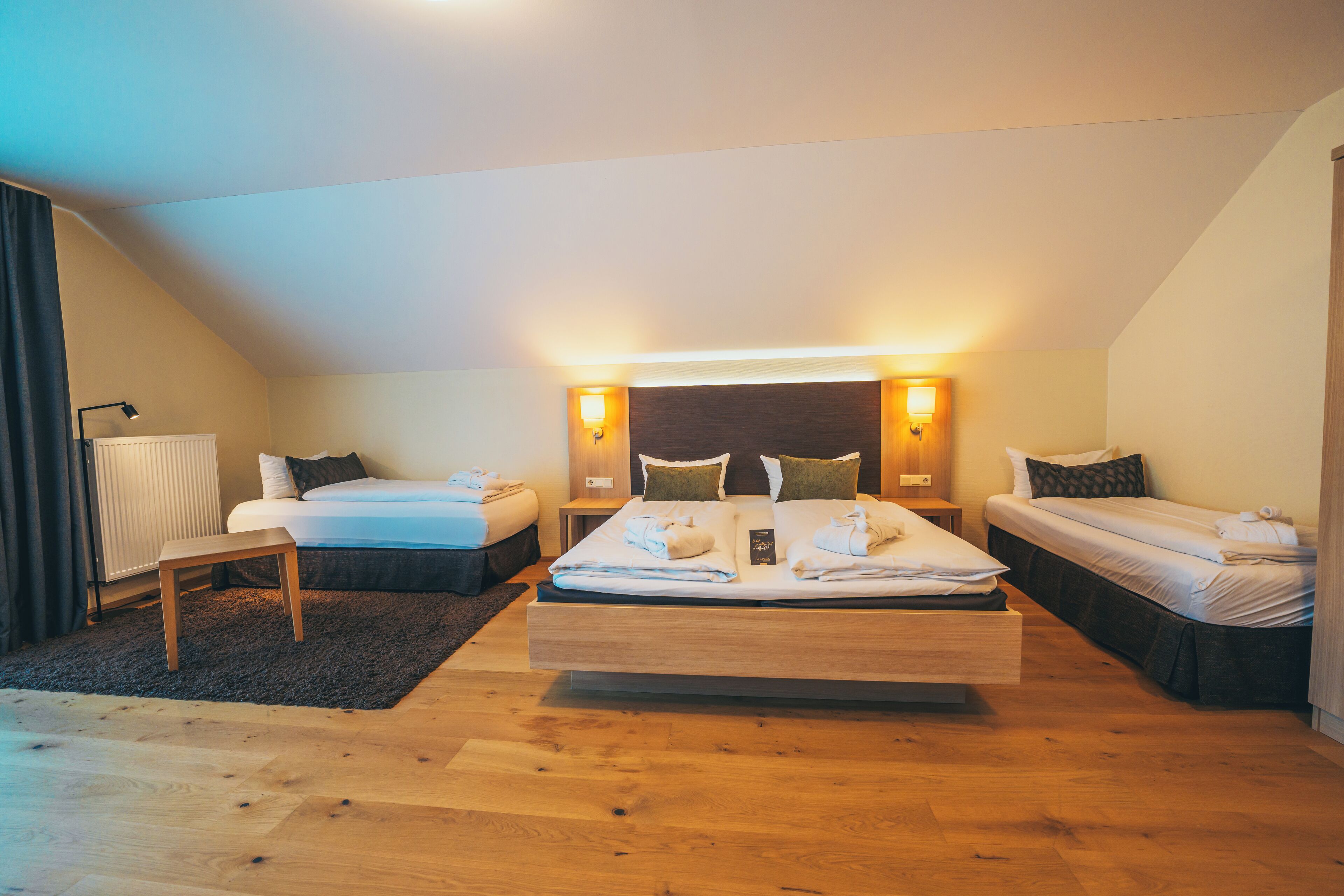 A bedroom with a large bed, two smaller beds, a wooden floor, and a radiator.