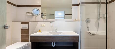 Un baño moderno con un lavabo blanco, un espejo, un inodoro y una ducha con mampara de cristal.