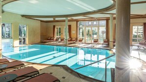 Una amplia piscina interior con techo iluminado por el sol y grandes ventanales.