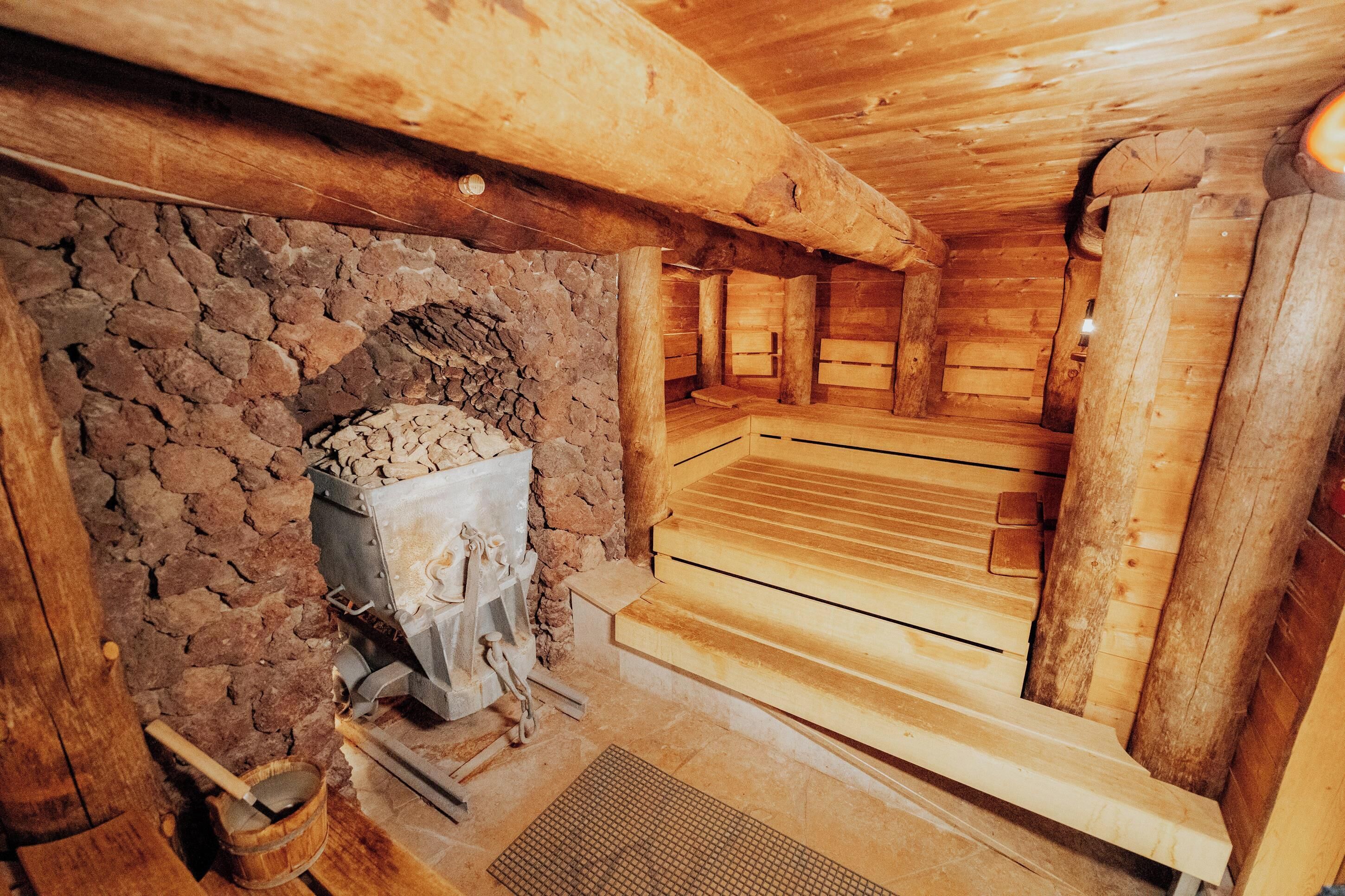 A sauna with a stone wall, wooden benches, and a stone heater.
