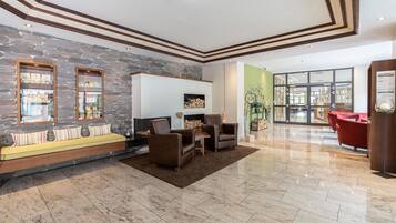 A spacious lobby with a stone wall, a seating area with sofas and armchairs, a fireplace, and a reception desk.