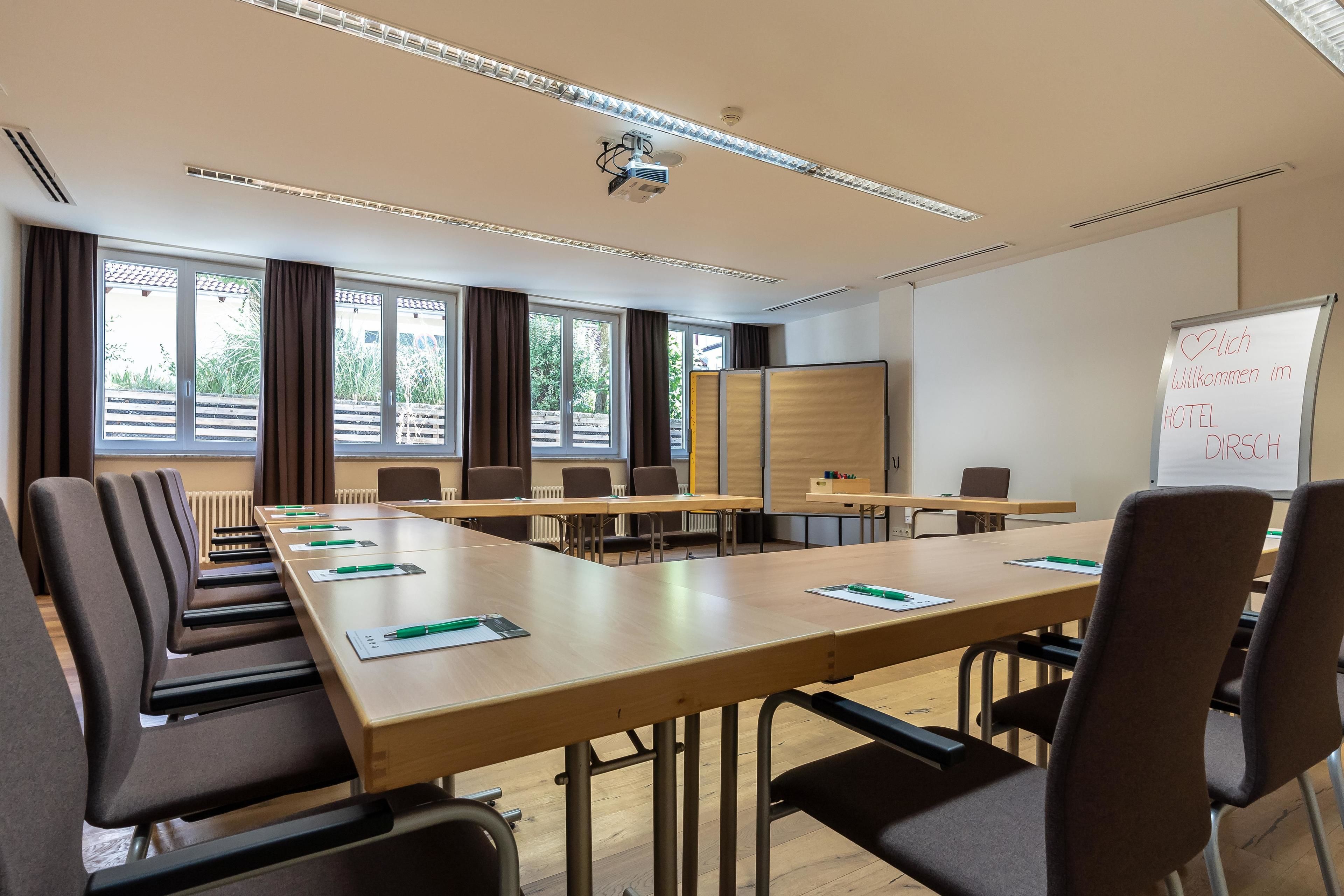 Ett konferensrum med långa bord, stolar, en whiteboard och en projektor.