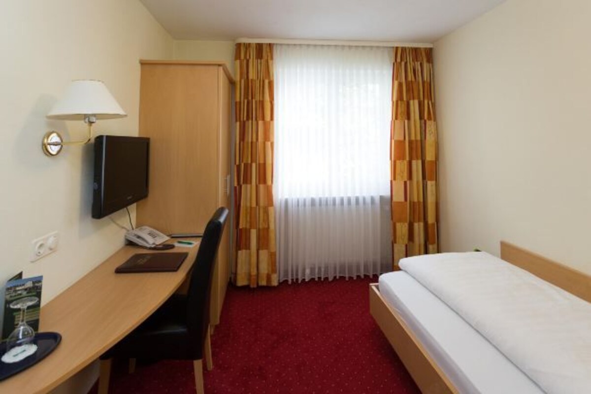 A hotel room with a single bed, a desk with a chair, a TV, and a telephone.