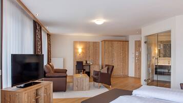 A modern hotel room with a flat-screen TV, a sofa, a chair, a small wooden table, and a bed.