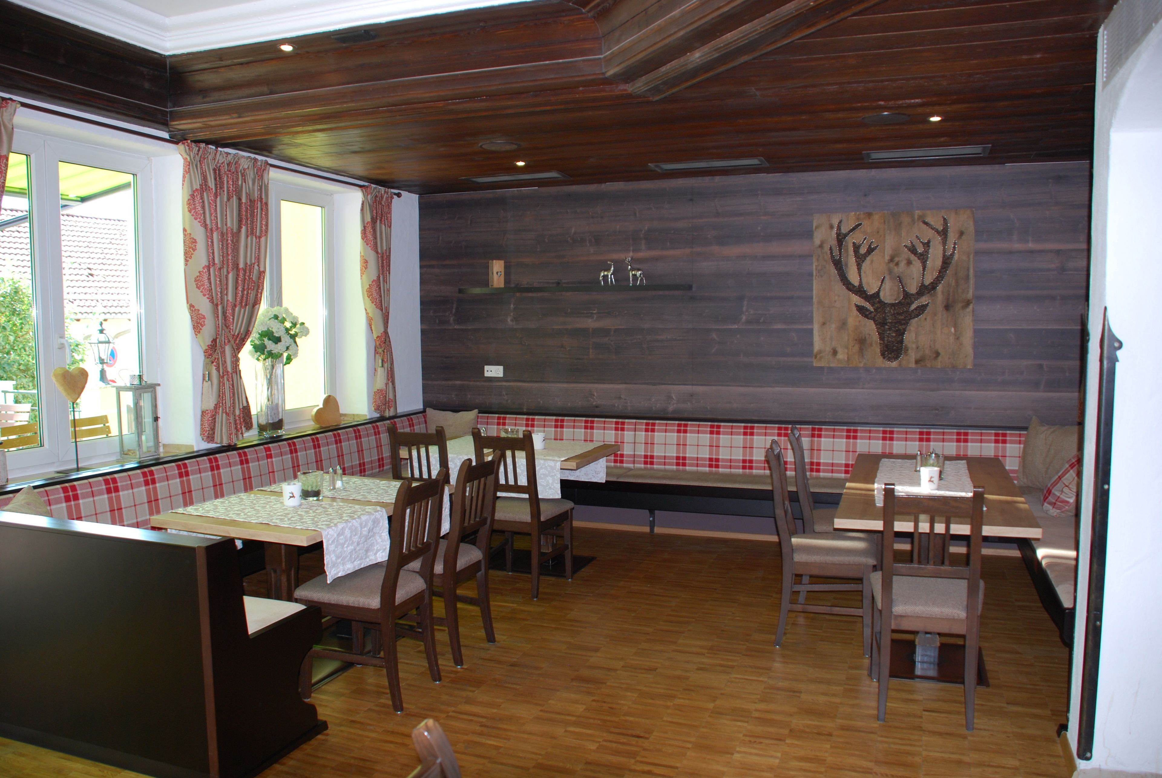Un restaurante con suelo de madera, asientos de banco a cuadros y una decoración de cabeza de ciervo en la pared.