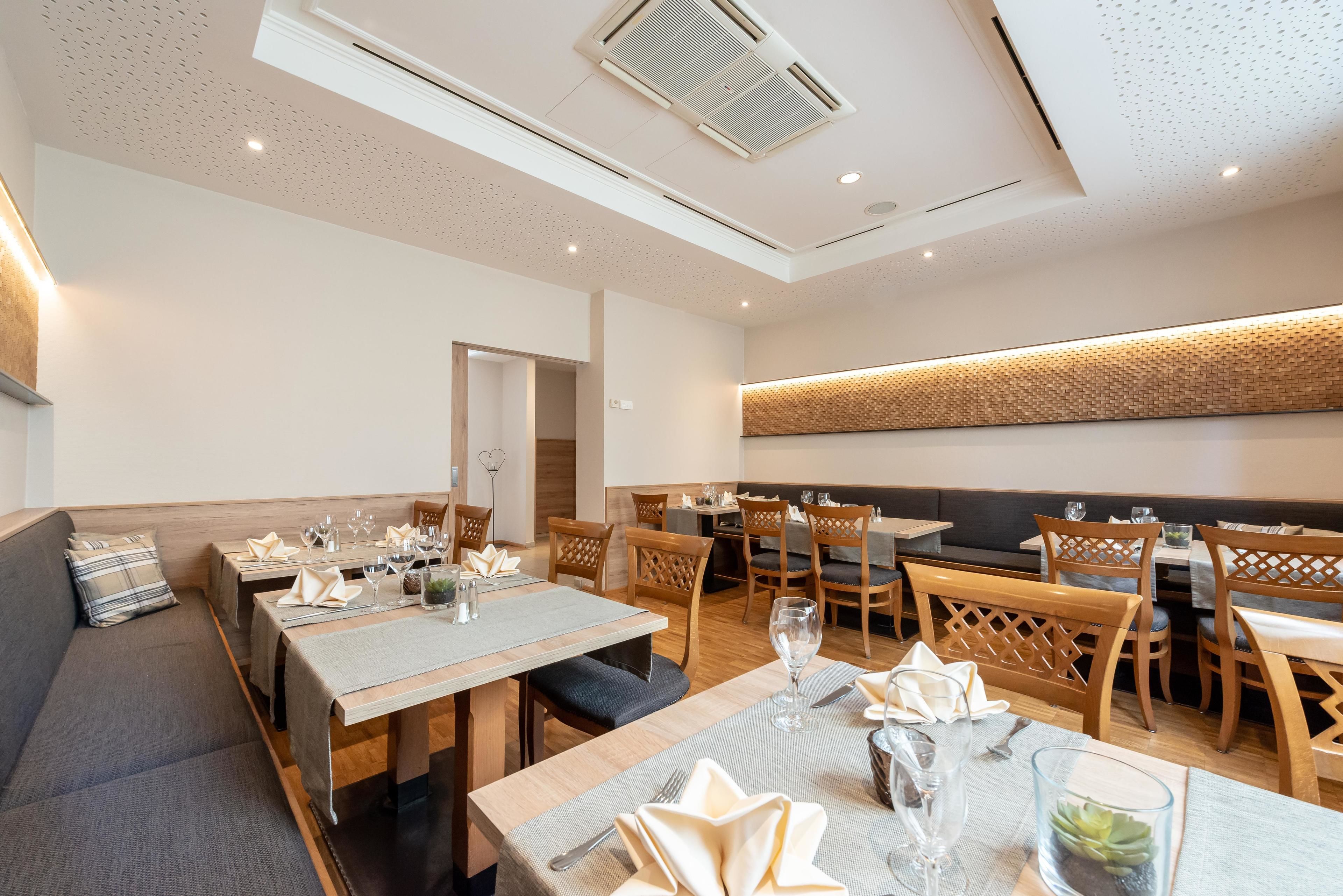A modern dining area with wooden tables and chairs, a grey sofa, and a patterned wall.