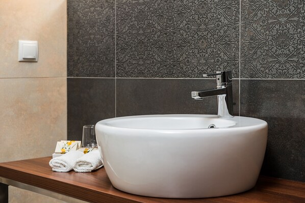 A white sink with a modern faucet on a wooden countertop, set against a dark patterned tile wall.