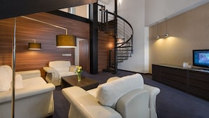A modern living room with a curved staircase, leather sofas, a coffee table, and a flat-screen TV. - Rado Resort Spa & Wellness (Mielec)