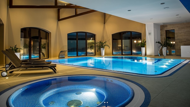 A large indoor swimming pool with a jacuzzi, lounge chairs, and potted plants. - Rado Resort Spa & Wellness (Mielec)