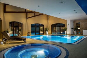 A large indoor swimming pool with a jacuzzi, lounge chairs, and potted plants.