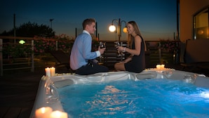 A couple sitting in a hot tub with candles and drinks, surrounded by a wooden deck and flowers. - Rado Resort Spa & Wellness (Mielec)