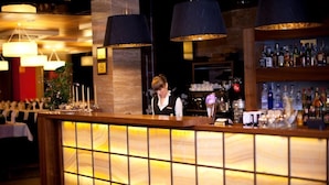 A bar area with a wooden counter, hanging blue lamps, and shelves with bottles. - Rado Resort Spa & Wellness (Mielec)