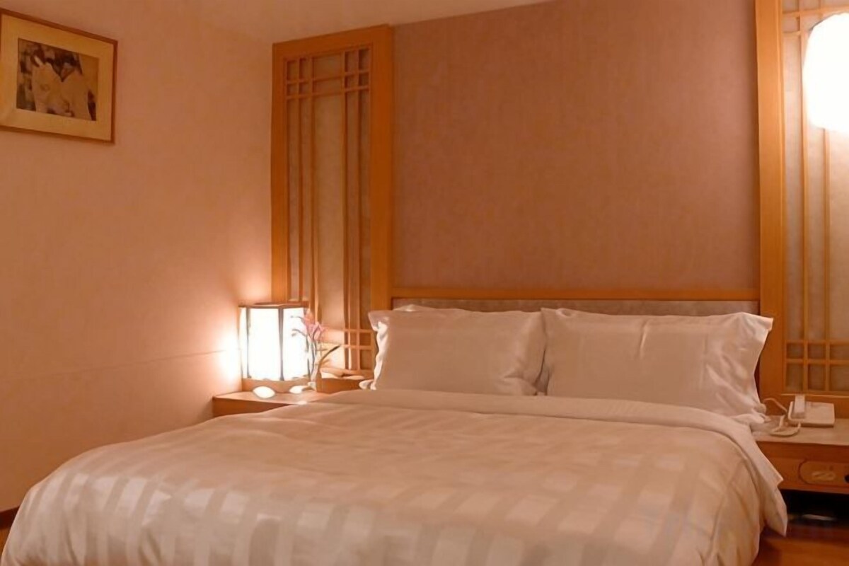 A hotel room with a bed, nightstand, lamp, and a framed picture on the wall.