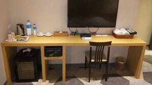 Habitación de hotel con escritorio de madera, televisor, refrigerador pequeño, silla y cesto de basura.