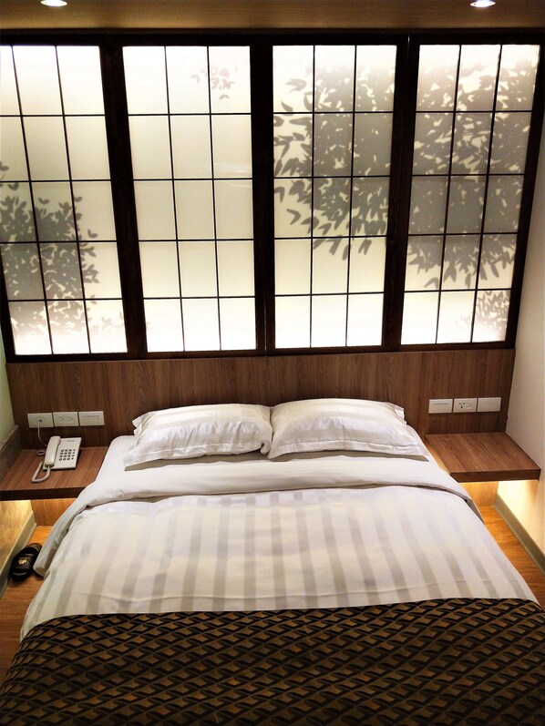 A hotel room with a bed, a bedside telephone, and a window with a view of trees.