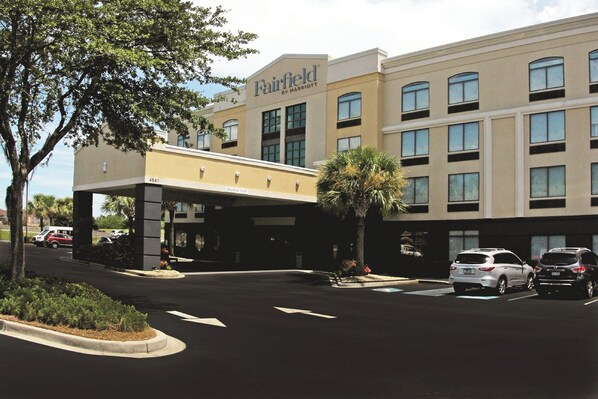 A hotel with a modern facade, multiple windows, and a parking lot with several cars.