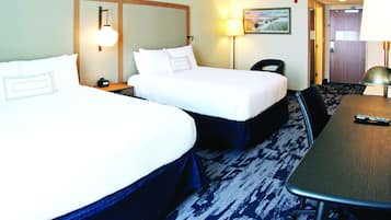 Une chambre d’hôtel avec deux lits, un bureau et une chaise. Il y a une lampe sur le bureau et un tableau au mur.