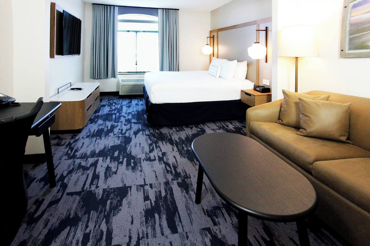 A hotel room with a bed, a desk, a sofa, a coffee table, a TV, and a window with curtains.