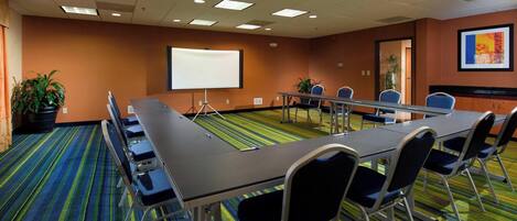 A conference room with a long table, chairs, a projector screen, and a carpeted floor.