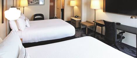 A hotel room with two beds, a desk, a chair, a TV, and a lamp.