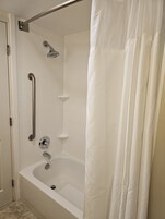 A bathroom with a white bathtub, a shower with a handheld showerhead, and a grab bar.