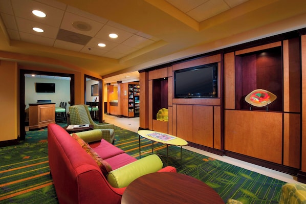 Un hall de hotel con zona de estar, televisor y mostrador de recepción.