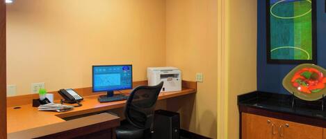 A reception desk with a computer, phone, and printer. There is a chair and a small desk area.